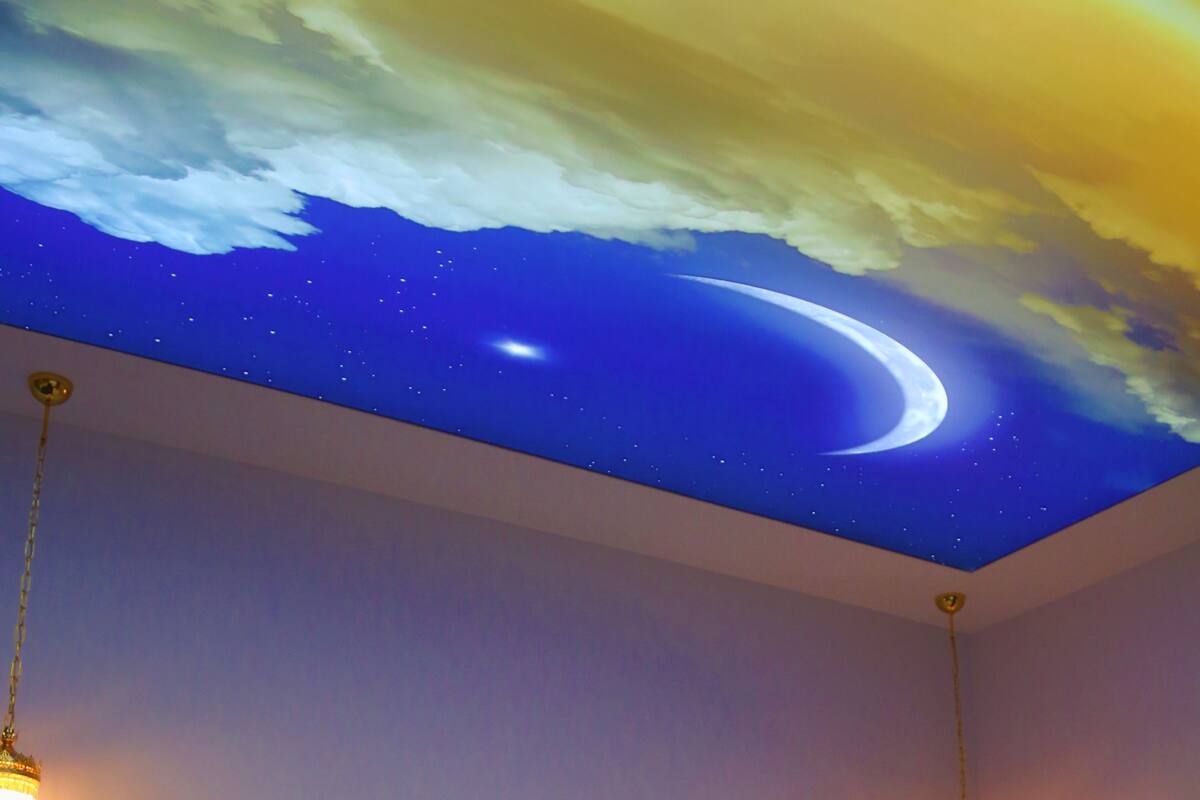 Quarto com cama, mesa de cabeceira e parede decorada com um mural do céu estrelado.