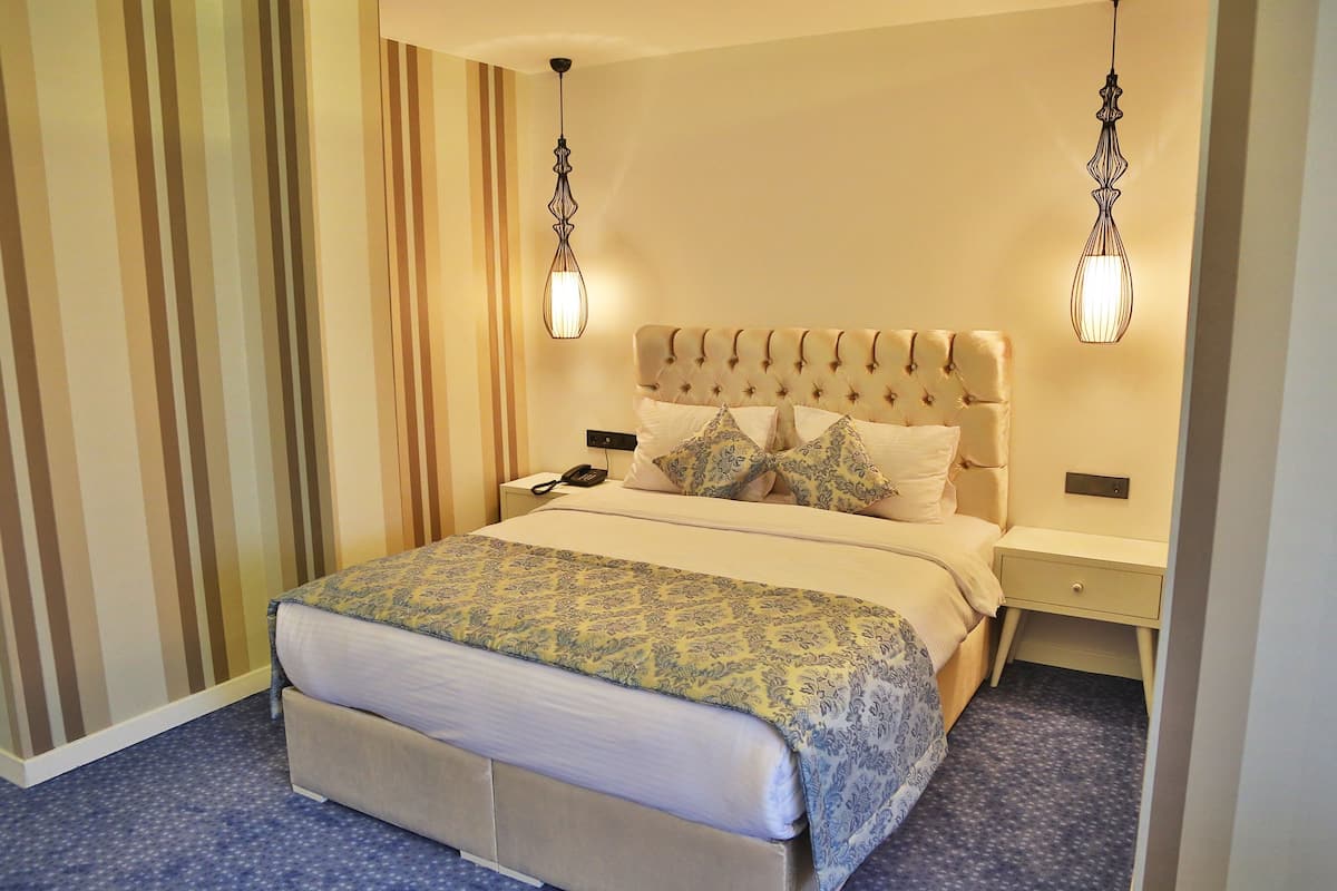 Quarto de hotel com cabeceira estofada, colcha estampada e duas luminárias de cabeceira.