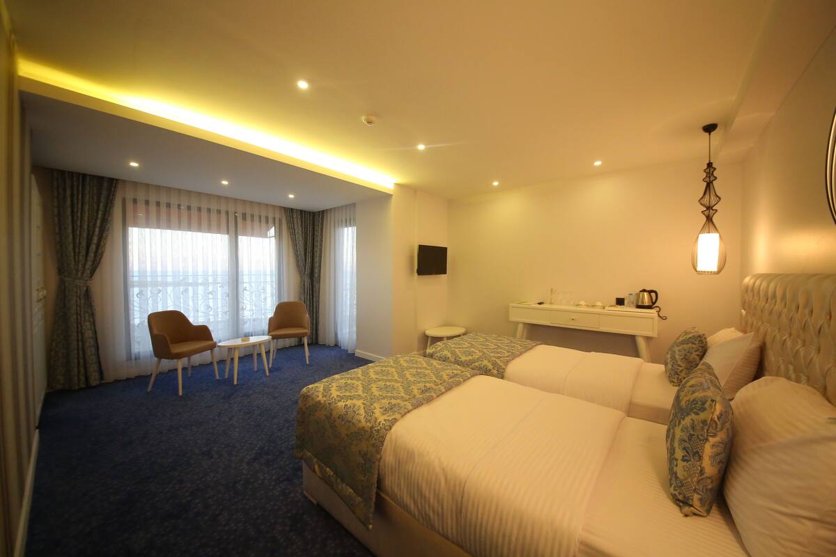 Quarto de hotel com uma cama grande, uma escrivaninha com cadeira, uma mesinha e uma televisão na parede.