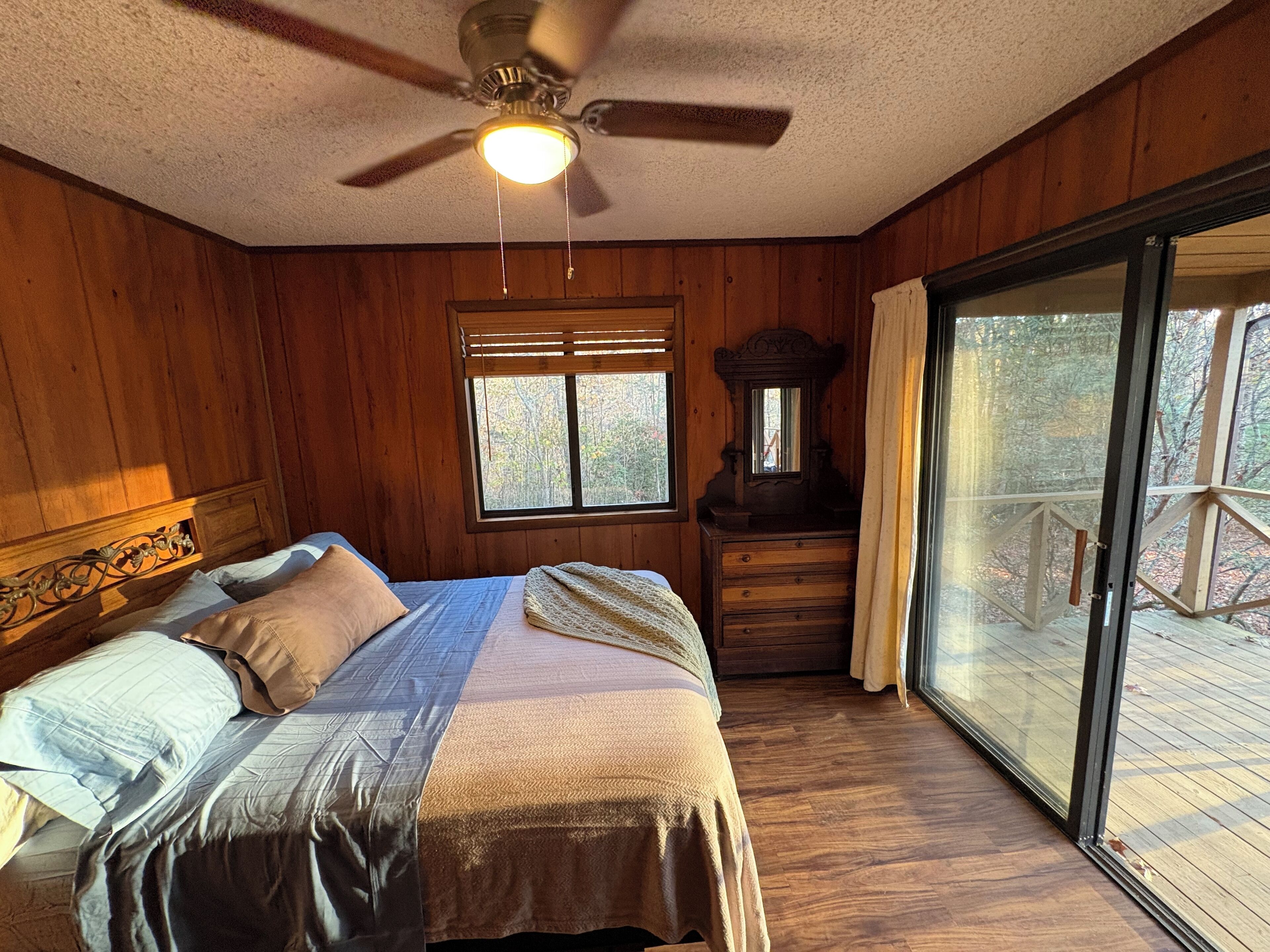 A bedroom with a bed, a dresser, a ceiling fan, a window, and a view of the outdoors.