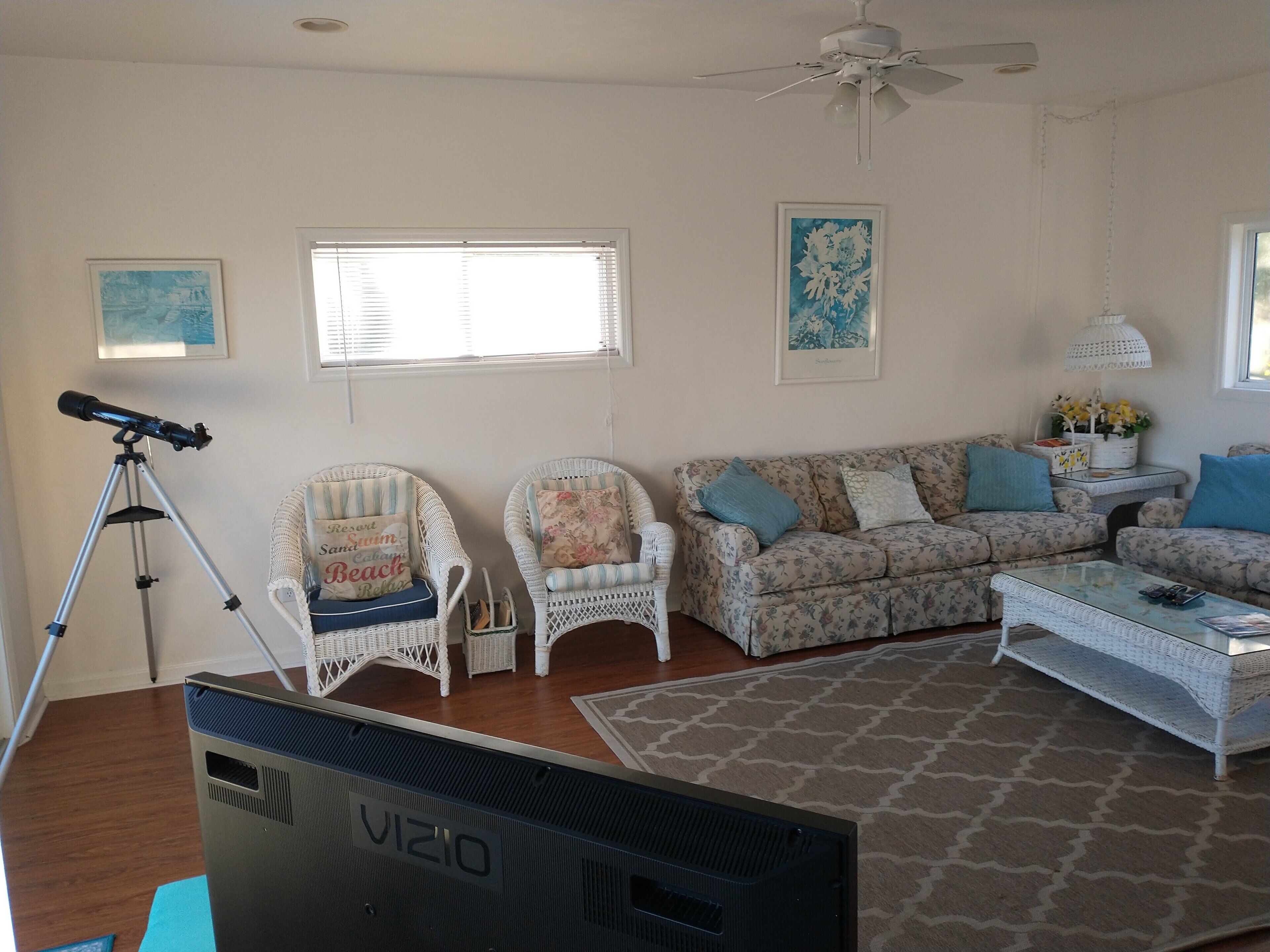 A living room with a telescope, two wicker chairs, a sofa, and a coffee table.