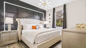 Un dormitorio moderno con cabecera capitonada, un ventanal con cortinas y una mesita de noche con lámpara.
