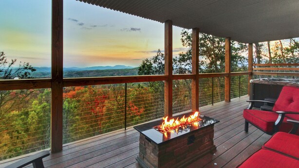 Um terraço com lareira e cadeiras vermelhas, com vista para uma paisagem montanhosa.