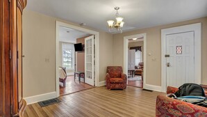 A spacious living room with hardwood flooring, a patterned armchair, a sofa, and a chandelier.