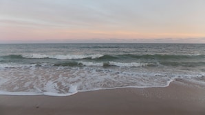 A beach with waves approaching the shore, a clear sky, and a calm sea.