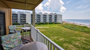 A balcony with outdoor seating overlooking a beach and a hotel building.