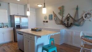 A kitchen with white cabinets, a stainless steel refrigerator, a wooden countertop, and a teal stool.