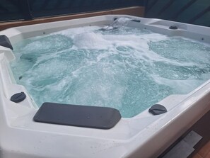 Ein Whirlpool mit sichtbaren Blasen und Wasserstrahlen, einem schwarzen Sitzplatz und einer Bedienkonsole.