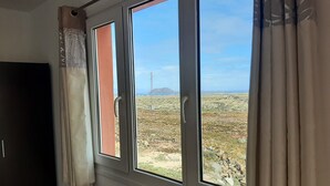 A room with a large window offering a view of a rocky landscape and a distant power line structure.
