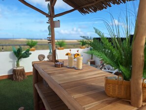 Une table en bois, avec deux boissons et un menu, entourée de plantes en pot et offrant une vue sur la plage.