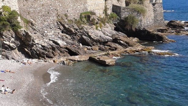 Une plage rocheuse aux eaux cristallines, un mur de pierres et une tour.