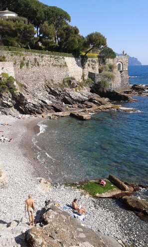A rocky beach with clear water, a stone wall, and a few people. - House in the green, 100 meters from the sea (Genova)