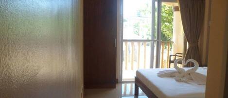 A hotel room with a bed, a balcony with a chair, and a view of the outside.
