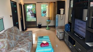 A living room with a sofa, a coffee table, a television, and a small table with a lamp. - Kitti Rose Home (Chiang Mai)