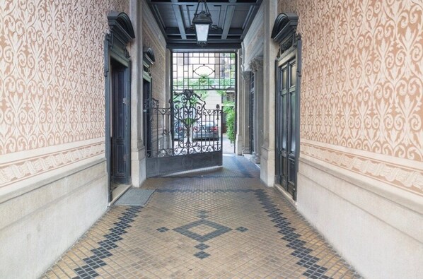 A corridor with patterned walls, a tiled floor, and a gate leading to a vehicle.