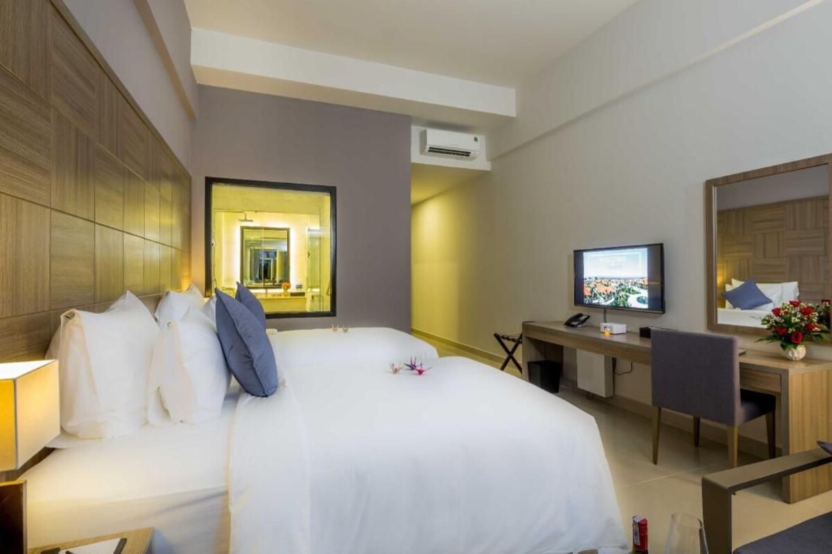 A hotel room with a bed, a desk, a television, and an air conditioning unit.