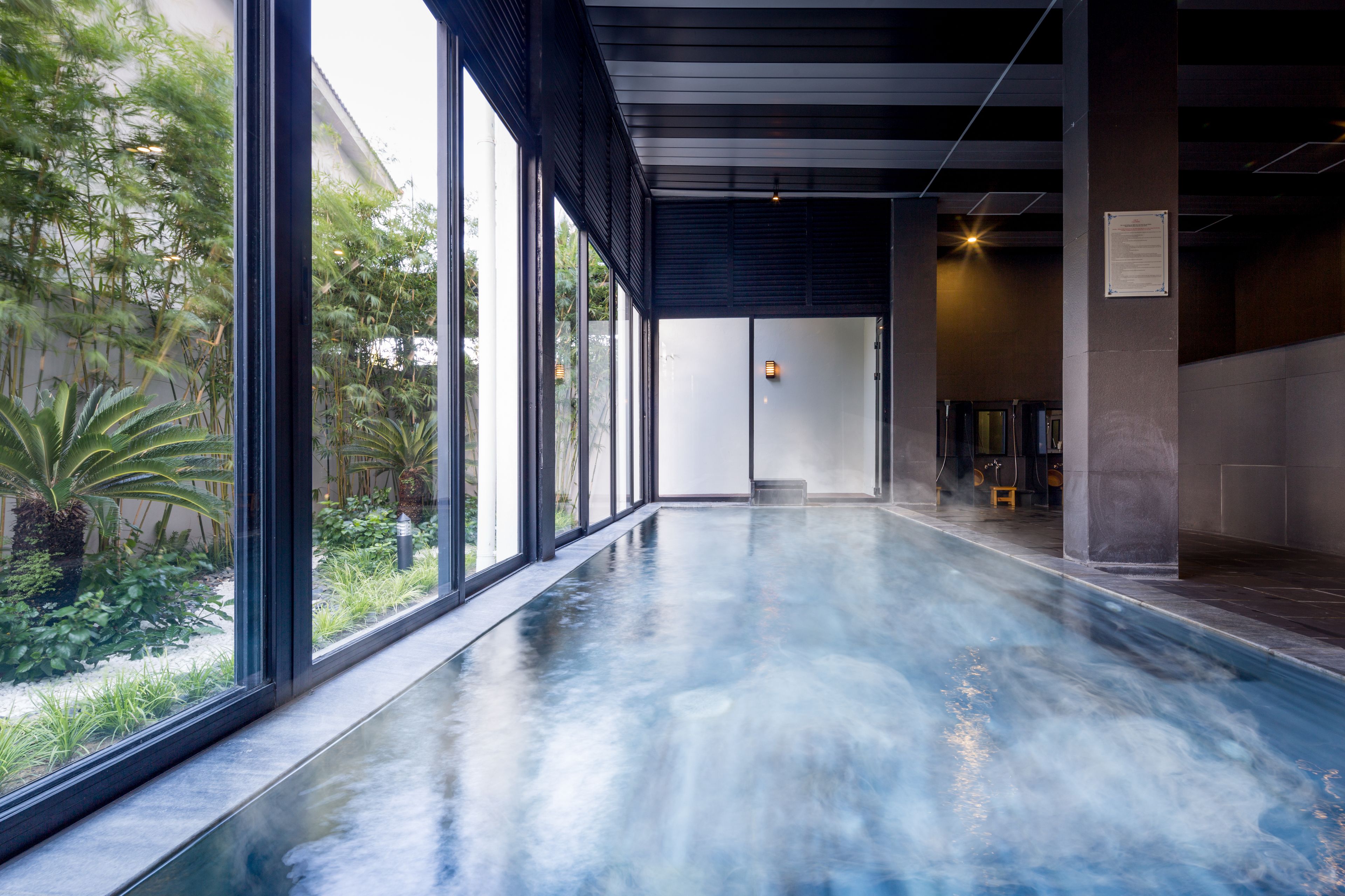 A spacious indoor pool area with large windows, a concrete floor, and a view of greenery outside.