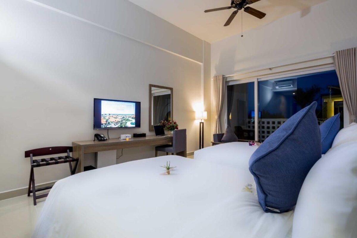 A hotel room with a bed, a desk with a computer, a TV, and a window with curtains.