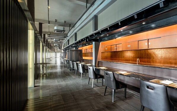 A modern restaurant with long tables and chairs, a wooden counter, and a tiled floor. - Grandvrio Ocean Resort Danang (Da Nang)