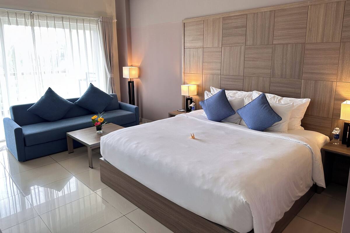 A hotel room with a large bed, a sofa, and two bedside tables with lamps.