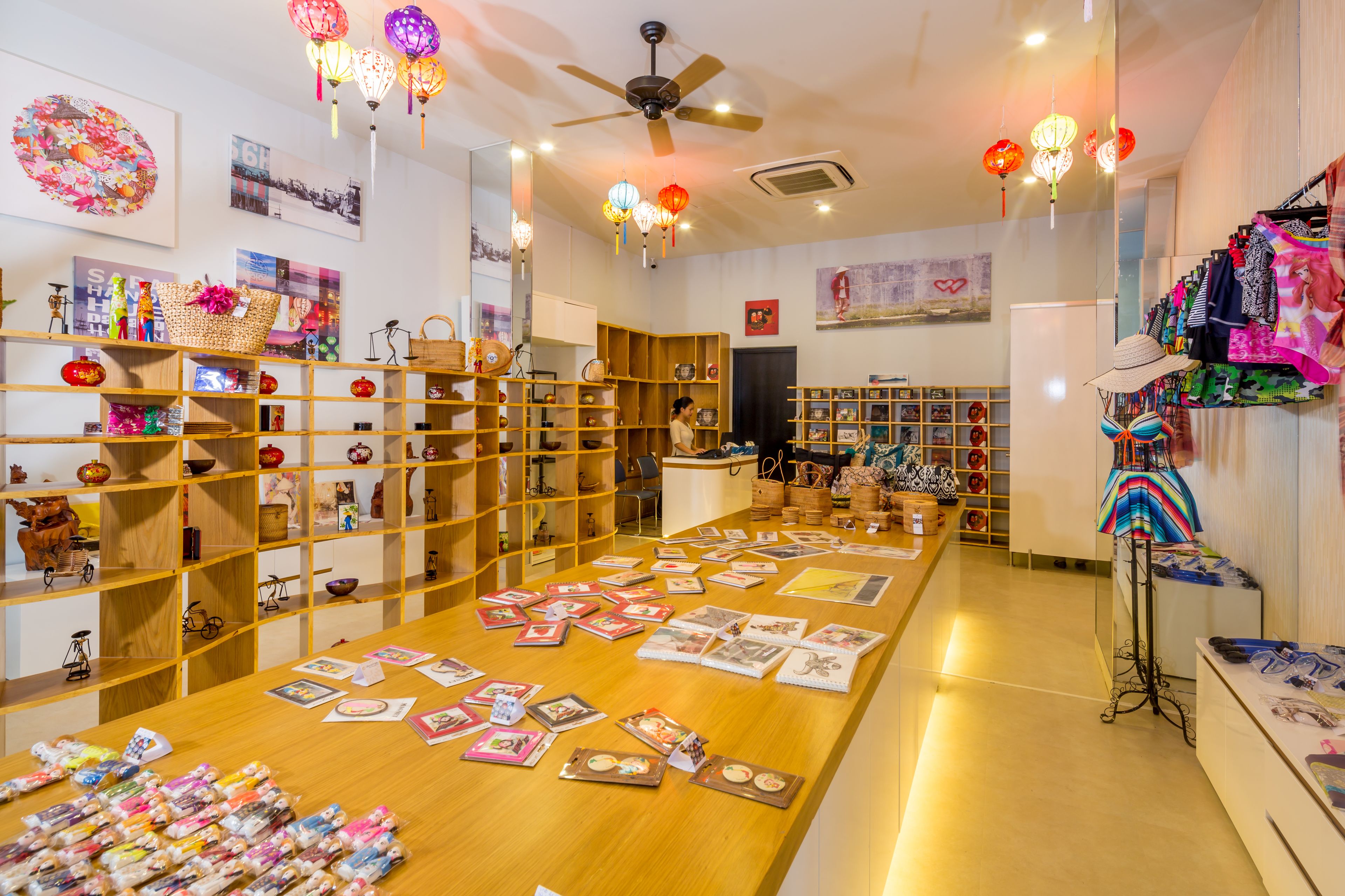 A spacious room with wooden shelves displaying various items, a central table with postcards, and a ceiling fan.