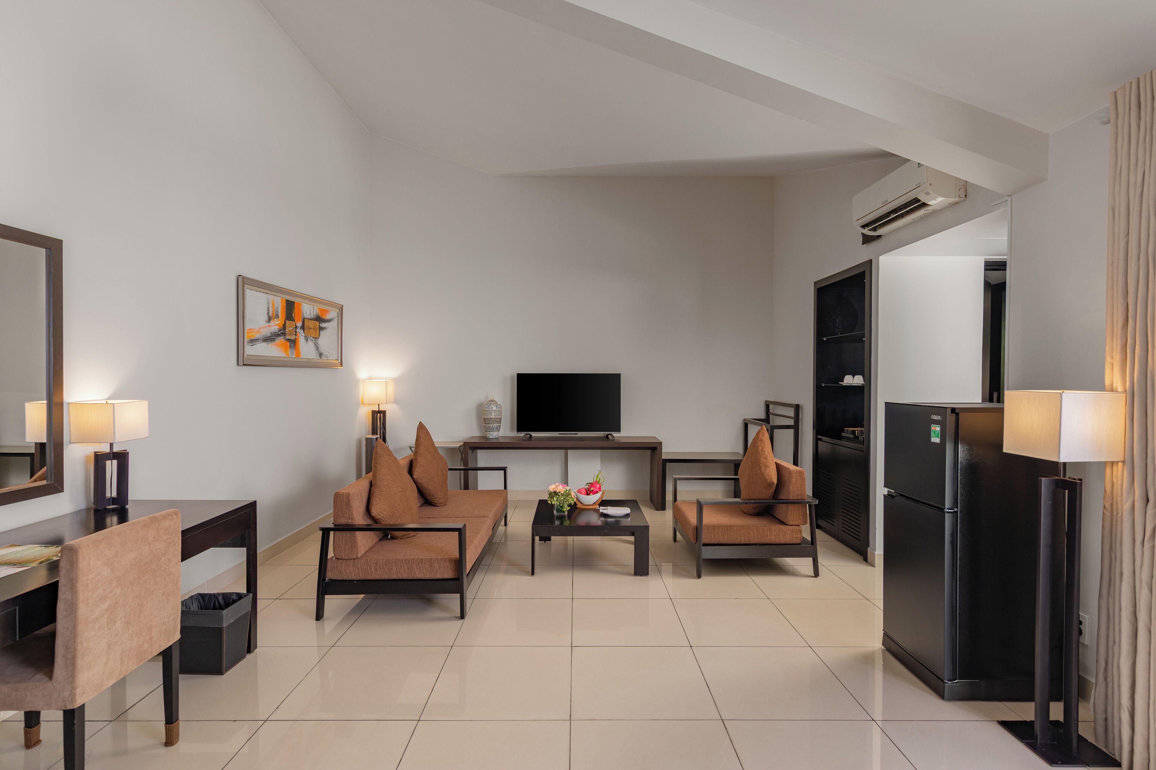 Una sala de estar moderna con un conjunto de sofás, una mesa de centro con flores, un televisor de pantalla plana y un refrigerador.