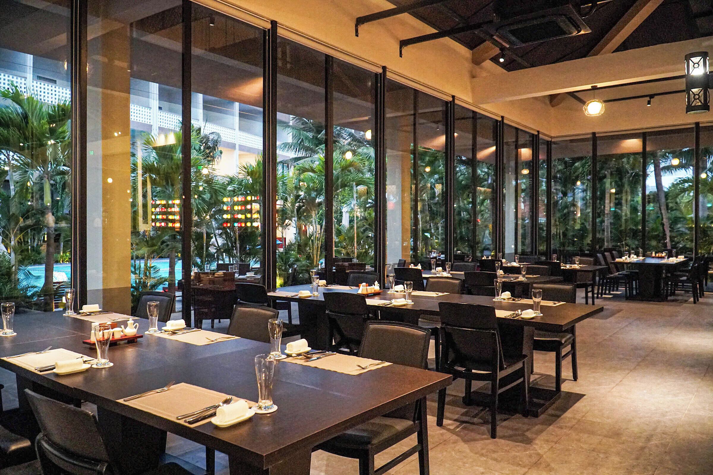 A restaurant with tables set for dining, large windows, and a view of palm trees.
