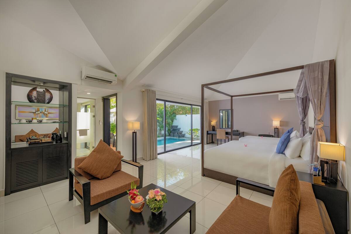 A spacious hotel room with a large bed, a sitting area with a coffee table, and a view of a swimming pool.