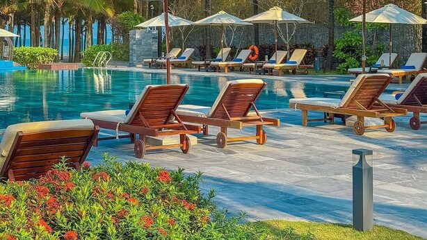 A poolside area with lounge chairs and umbrellas, surrounded by palm trees. - Grandvrio Ocean Resort Danang (Da Nang)