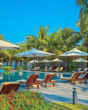 A poolside area with lounge chairs and umbrellas, surrounded by palm trees. - Grandvrio Ocean Resort Danang (Da Nang)
