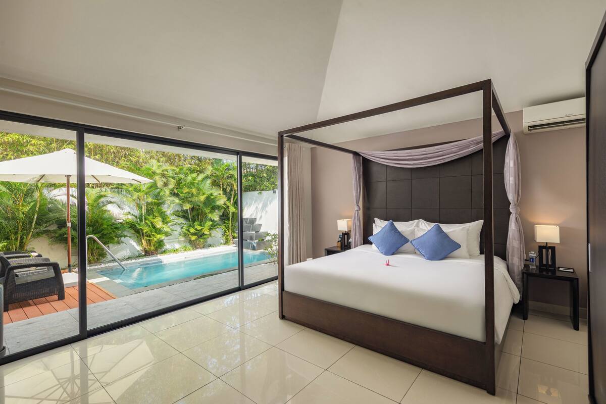 A spacious bedroom with a large bed, a view of a swimming pool, and a balcony with outdoor furniture.