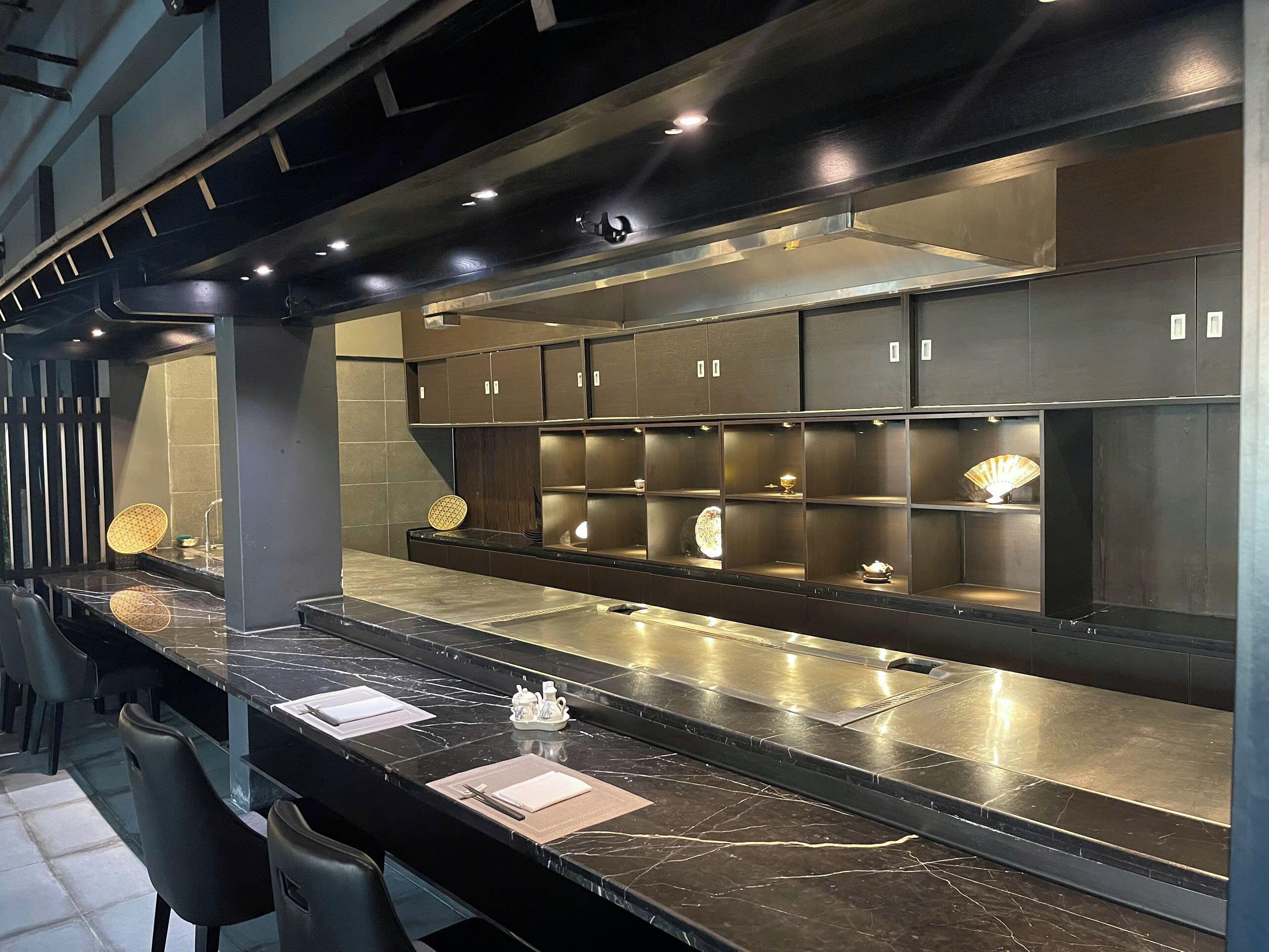 Un área de bar moderna con una barra larga, encimera de mármol negro y varias sillas.