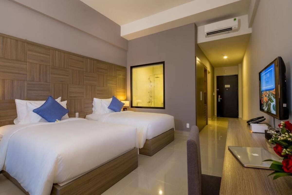 A hotel room with two beds, a desk with a laptop, a TV, and a framed artwork on the wall.