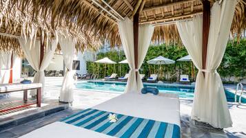 Relax by the serene pool surrounded by lounge chairs and umbrellas, under a thatched roof structure.