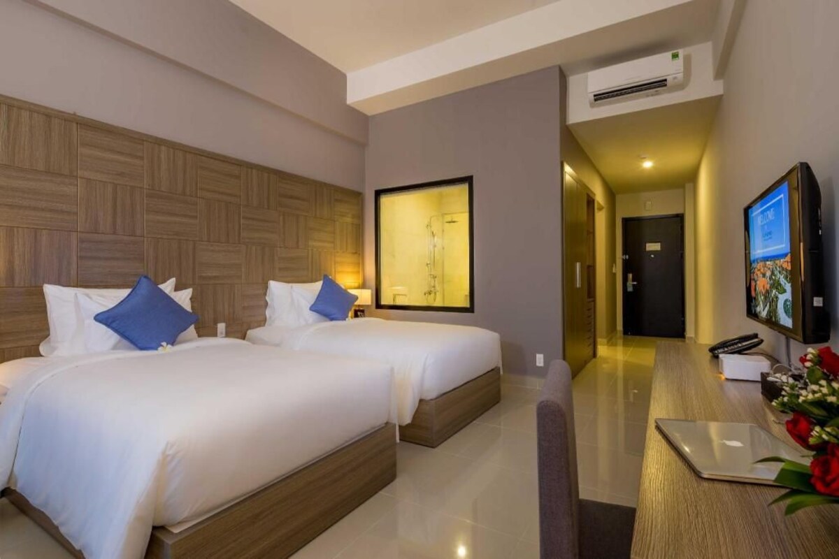A hotel room with two beds, a desk with a laptop, a TV, and a framed artwork on the wall.