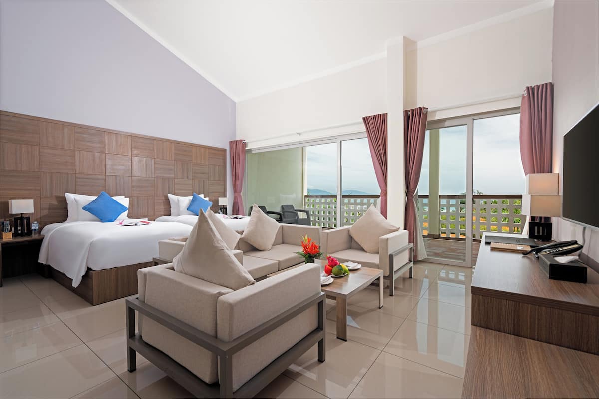 A hotel room with a bed, two sofas, a desk, and a balcony with a view.