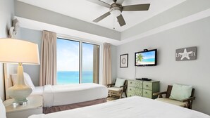 Habitación de hotel con dos camas, un ventilador de techo, televisor y vista al océano.