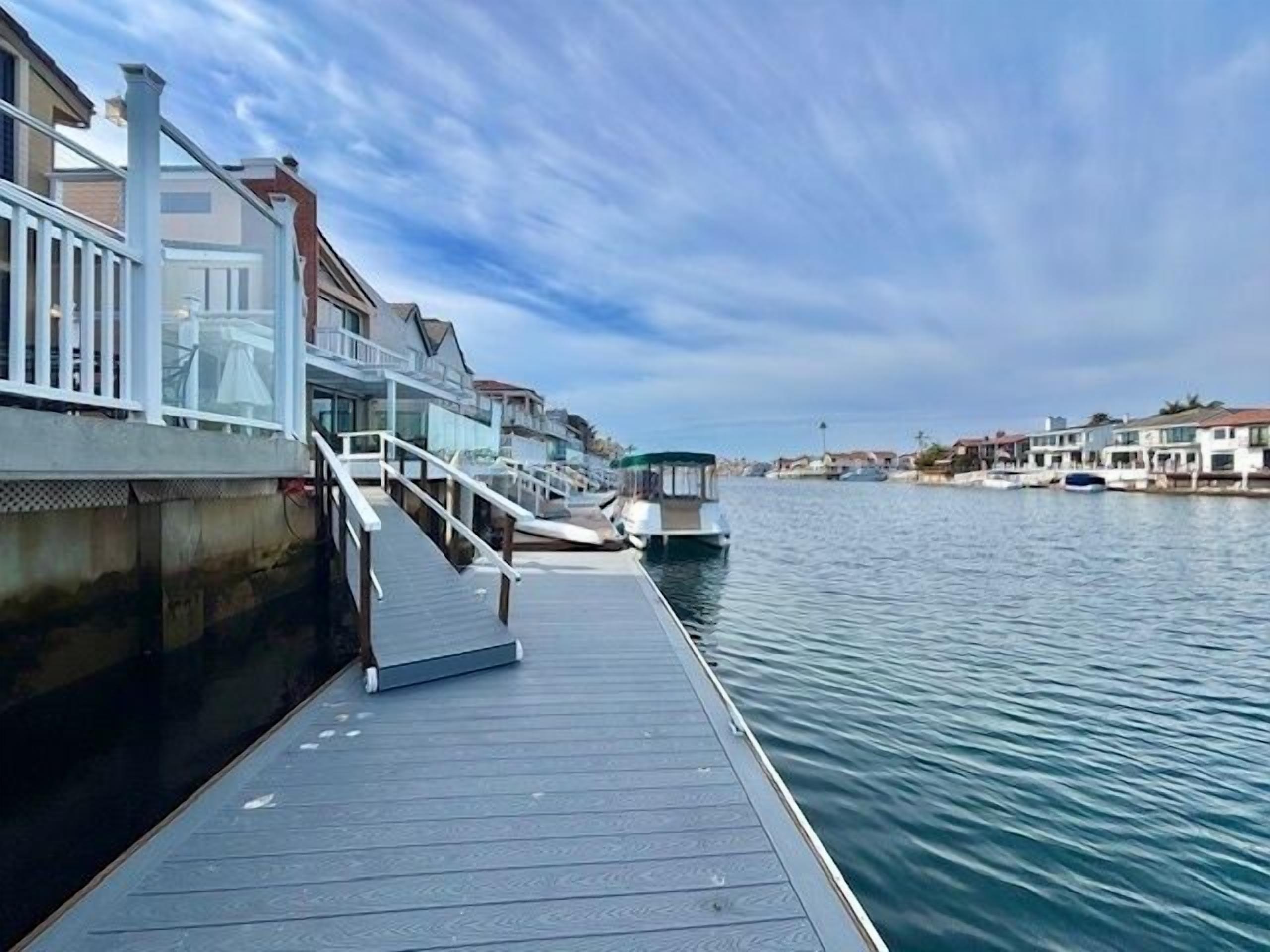 A waterfront dock with a wooden walkway leading to a building with a white railing.
