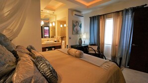 Een slaapkamer met een groot bed, een bureau, een stoel en een badkamer zichtbaar door een geopende deur.