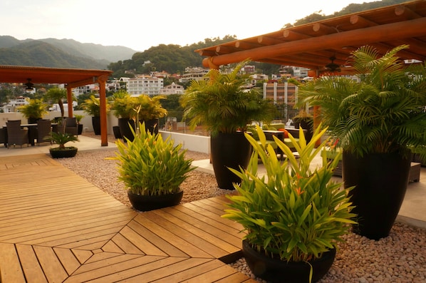 A rooftop terrace with potted plants, wooden flooring, and outdoor furniture.