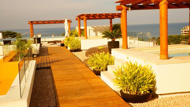 Een dakterras met houten vloerdelen, planten in potten en een pergola.