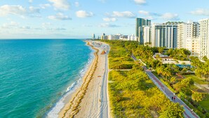 Un paisaje urbano costero con una playa, edificios altos y un camino peatonal junto a la playa.