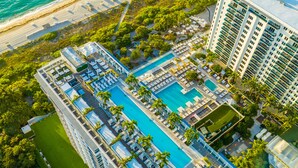 Vista aérea de un complejo turístico con varias piscinas, una playa y edificios de gran altura.