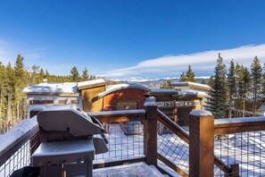 A snow-covered outdoor area with a wooden fence, a grill, and a view of cabins in the background.