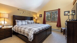 A bedroom with a bed, nightstands, a dresser, a window with curtains, and a wall-mounted lamp. - Secluded Getaway: Private Hot Tub & Forest Views (Breckenridge)