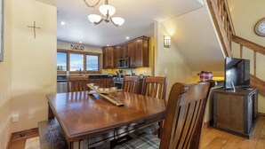 A dining area with a wooden table and chairs, a chandelier, and a kitchen in the background. - Secluded Getaway: Private Hot Tub & Forest Views (Breckenridge)