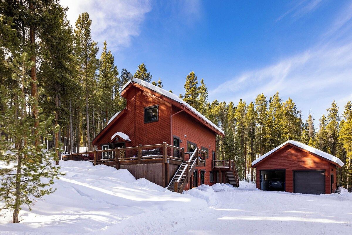 Eine Holzhütte mit überdachter Terrasse und Garage, umgeben von Schnee und Bäumen.