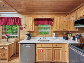 A compact kitchen with wooden cabinets, a built-in dishwasher, a coffee maker, and a microwave. - Gatlinburg | Pool Table | WiFi | Fireplace | Hot Tub (GATLINBURG)