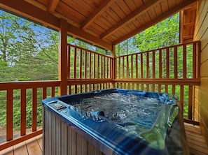 A hot tub on a wooden deck with a view of green trees.