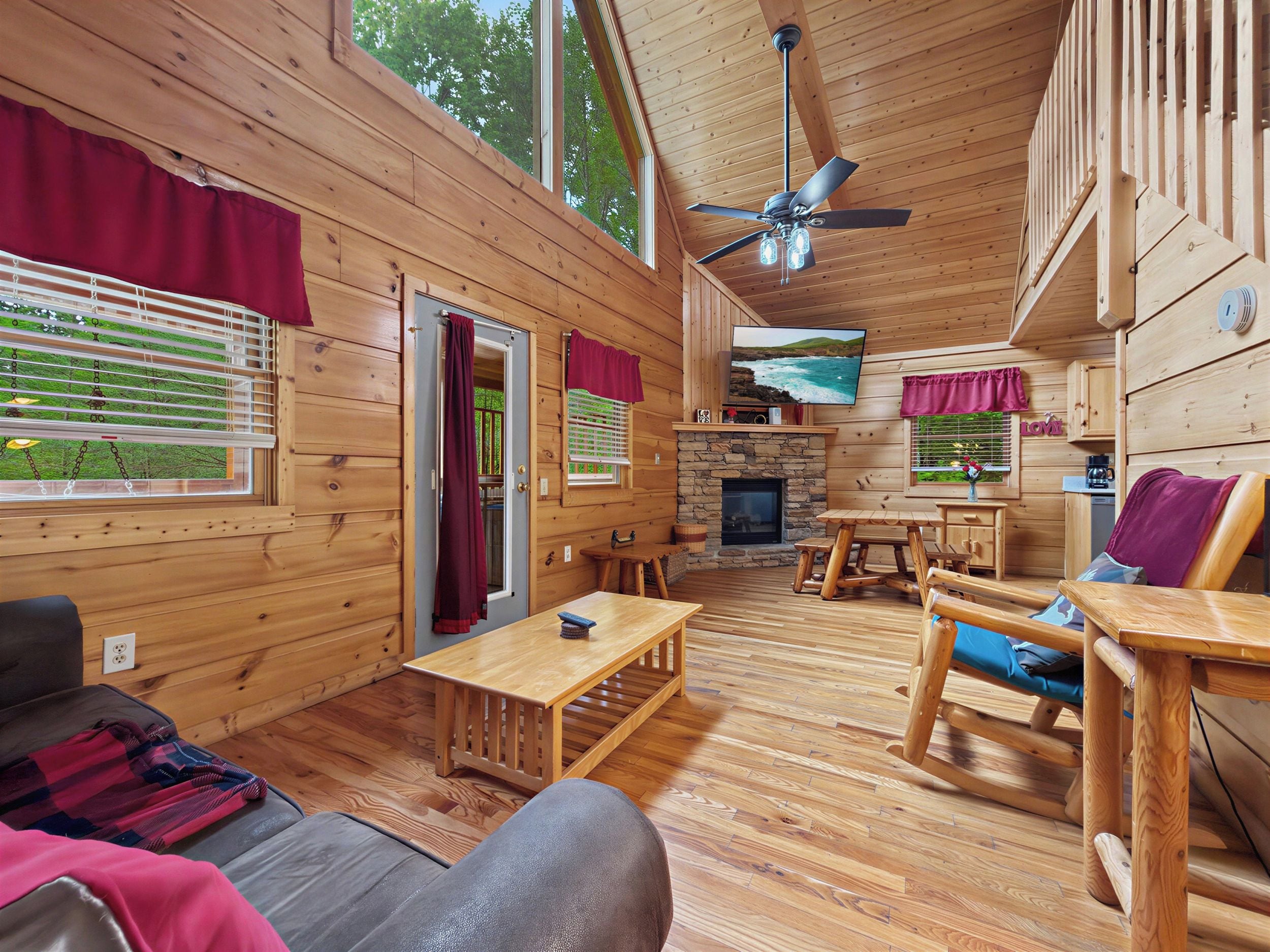 A wooden cabin interior with a fireplace, wooden furniture, and large windows.